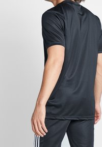 Camiseta atlética negra de manga corta en una tela suave, con cuello redondo y un diseño ajustado. Sin logotipos ni patrones visibles.