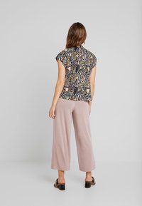 Blouse à manches courtes avec imprimé animal multicolore, associée à un pantalon large rose clair. Caractérisée par une coupe décontractée et une texture douce.