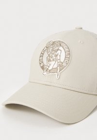 Beige baseballcap med teksturert stoff, med en brodert Boston Celtics-logo i sølv, buet skygge og mesh-back.