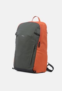 Sac à dos avec un extérieur vert et orange, comportant une poignée supérieure, une poche zip latérale et des bretelles noires réglables pour le confort et l'utilité.
