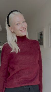 Burgundi meilinis suknelis, minkšta tekstūra, prigludęs dizainas, ilgomis rankovėmis, dėvimas su juodu plaukų juostele; minimalistiška fono aplinka su įrėmintomis nuotraukomis.