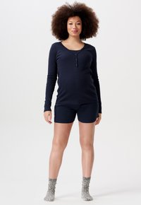 Granatowa bluzka z długim rękawem, dekoltem w serek i detalami guzików, w połączeniu z granatowymi szortami. Model nosi teksturowane, szare skarpetki sięgające do kolan. Proste tło.