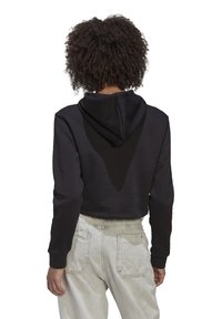 Svart hoodie med dragsko på huvan, mjuk textur, åtsittande ärmar och ett V-format designdetalj på baksidan, tillsammans med ljusa jeans i denim.