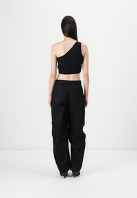 Femme aux longs cheveux foncés, de dos, portant un crop top noir asymétrique, un pantalon large noir et des chaussures à talons noires.