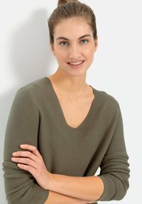 Oliwkowy, prążkowany sweter dziany z dekoltem w kształcie litery V i długimi rękawami. Materiał ma teksturowane wykończenie, z dopasowanymi mankietami i luźnym krojem.
