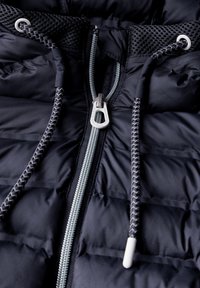 Giacca puffer navy con zip frontale, stringhe intrecciate e dettagli in rete. La texture a trapunta offre isolamento e un design sportivo.