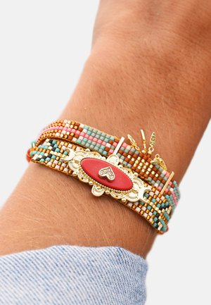 Bracelet multicolore en perles avec un accent doré, une pierre rouge centrale ornée d'un motif en forme de cœur, et des détails métalliques.