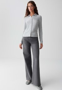 Camicia button-up grigia chiara a coste con colletto, abbinata a jeans a zampa d'elefante grigi scuri e scarpe slip-on grigie. Design semplice, tessuto texturizzato.