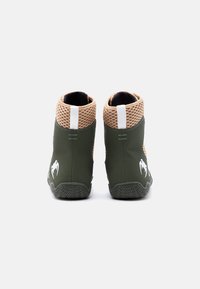 Ζευγάρι αθλητικών παπουτσιών ψηλού πάνω μέρους σε πράσινο και μπεζ χρώμα με ύφασμα δίχτυ και λευκές θηλιές για τράβηγμα, σε οπίσθια προβολή πάνω σε λευκό φόντο.