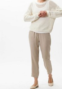 Pull en tricot crème à la coupe ample, associé à un pantalon beige ajusté et des ballerines de couleur claire, présentant une silhouette décontractée.