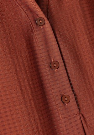 Ruskean värinen nappipaita, jossa on tekstuurilla varustettu kuvio, pyöreät ruskeat napit ja pehmeä, kevyt kangas.