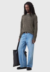 Olive green knit sweater, loose-fitting light blue jeans, black belt, black bag, black slip-on shoes. Textured fabric and relaxed silhouette.
