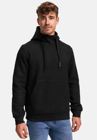 Hoodie noir en tissu texturé, avec poche kangourou, capuche à cordon de serrage réglable et poignets côtelés. Design décontracté, associé à un jean bleu.