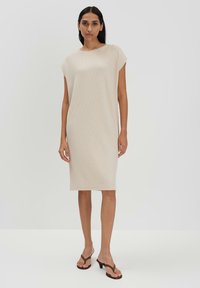 Beige Strickkleid mit kurzen Ärmeln, geradem Schnitt, knielang, glatte Textur. Getragen mit braunen Absatz-Flip-Flops, minimalistisches Design.