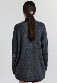 Maglione grigio oversize a maglia con maniche lunghe, caratterizzato da occhielli argentati sulle maniche e un aspetto strutturato, mostrato da dietro.