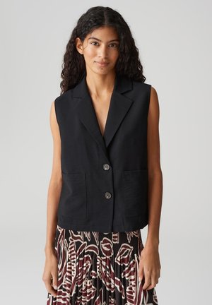 Blazer senza maniche nero con rever a punta, due tasche anteriori a toppa e due bottoni. Tessuto dalla texture liscia, design minimal.