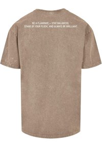 Camiseta marrón de manga corta con cuello redondo. Presenta una tela con textura y un diseño de texto impreso en blanco en la parte posterior.