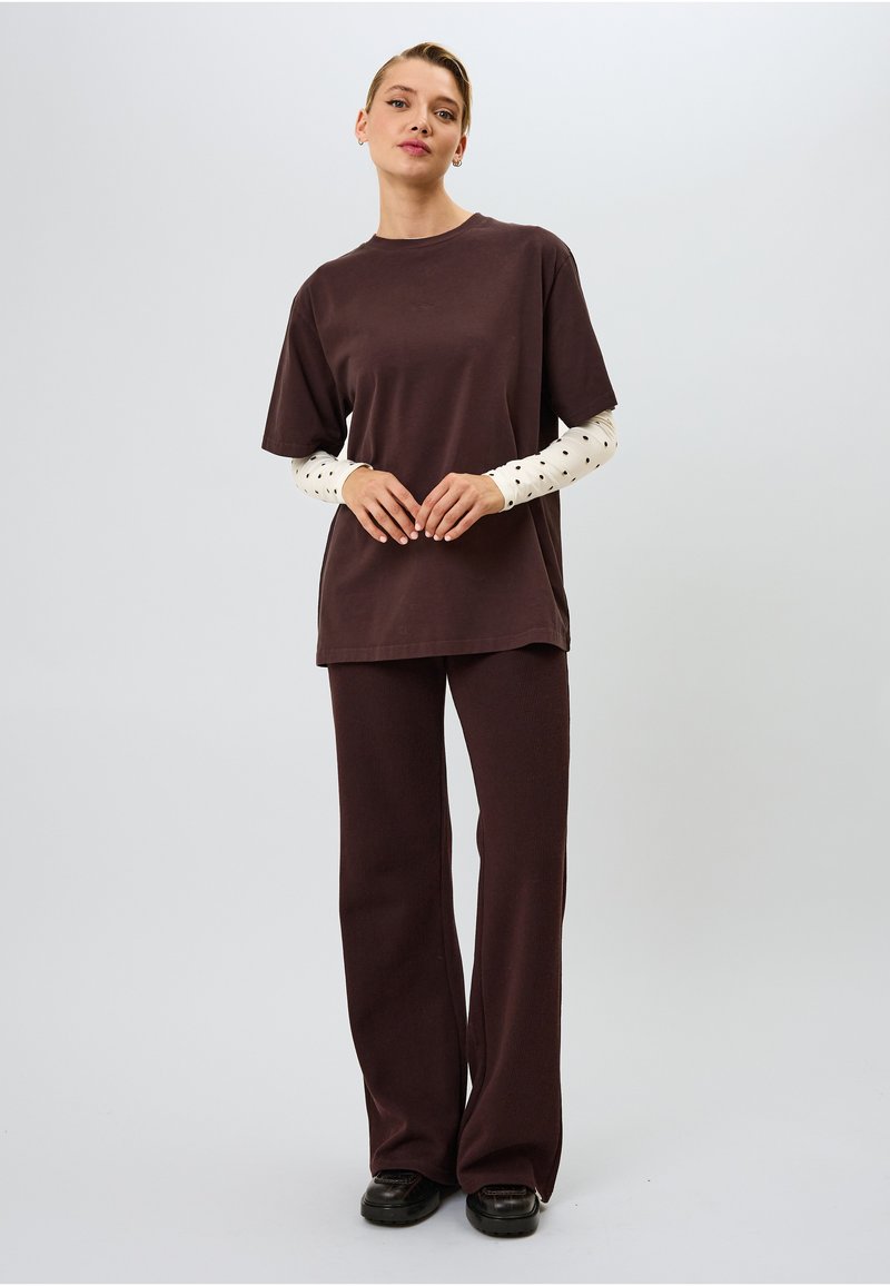 Tummanruskea ylisuuri t-paita, paritettu ribbitettyjen ruskeiden housujen kanssa, joissa on valkoinen pitkähihainen paita mustilla pilkuilla alla; sileä kangas.