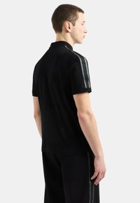 Polo nero a maniche corte, con accenti a righe grigie sulle spalle. Realizzato in un tessuto morbido e leggero.