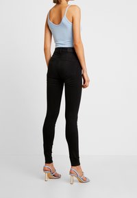 Jeans negros ajustados de cintura alta, combinados con una camiseta de tirantes de ribete azul claro y tacones de tiras azul claro, que resaltan su textura suave y su ajuste.