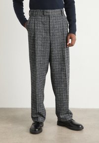Pantaloni în carouri gri și negre, cu talie înaltă, pliseuri și buzunare laterale, confecționați dintr-un material texturat. Asortați cu pantofi negri.