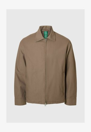 Veste marron à fermeture éclair avec col pointu, manches longues et texture lisse ; présente une étiquette verte visible au niveau du col.