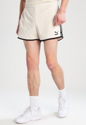 Beige sportshorts met een zwarte rand, voorzien van een zijlogo en gestreepte accenten. Gemaakt van lichte, ademende stof.