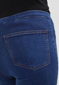Jeans de mezclilla azul oscuro con una cinturilla suavemente acabada, un bolsillo trasero con costuras contrastantes y un ajuste ceñido.