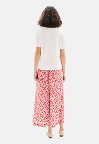 Haut blanc à manches courtes associé à un pantalon ample rouge à fleurs avec un motif floral blanc, en tissu doux et à coupe décontractée.