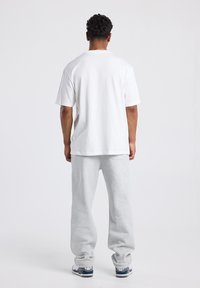 Camiseta de algodón blanca de manga corta, combinada con pantalones de chándal gris claro, con un corte relajado y cinturilla elástica.