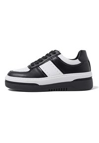 Sneaker bianco e nero con tomaia in pelle liscia, punta perforata e suola nera spessa. Presenta strisce laterali a contrasto e accenti testurizzati.