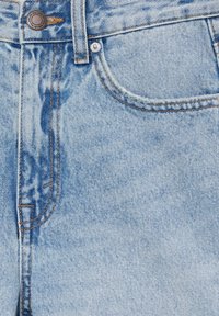 Jeans de mezclilla azul claro con una textura ligeramente desgastada, costuras naranjas y un botón plateado en la cintura, con un detalle de bolsillo frontal.