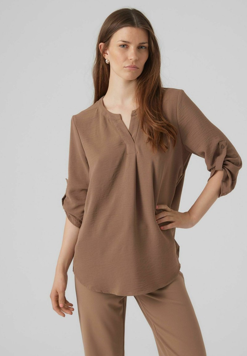 Camicia marrone con colletto e maniche arrotolate, realizzata in tessuto leggero. Abbinata a pantaloni marroni coordinati, con vestibilità rilassata.