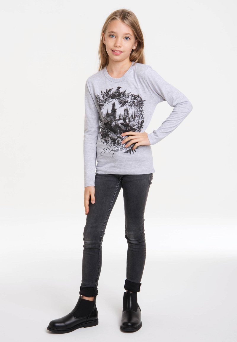 Gray long-sleeve shirt featuring a black design of a castle and foliage. Paired with dark jeans and black ankle boots.