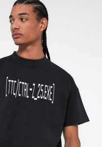 Μαύρο βαμβακερό μπλουζάκι με γραφικό σχέδιο σε λευκό: "[TTC/CTRL-Z_25.EXE]" στο μπροστινό μέρος; άνετη εφαρμογή με στρογγυλή λαιμόκοψη.