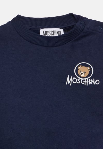 T-shirt côtelé bleu marine à col rond avec étiquette Moschino et logo nounours imprimés près de l'encolure côté droit.