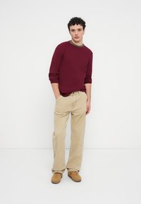 Μπορντό ριμπ μπλούζα με μακριά μανίκια, λαιμόκοψη σε ελιάς χρώμα; μπεζ παντελόνι από κορδούρα; καφέ αθλητικά παπούτσια; άνετη εφαρμογή, απλός σχεδιασμός, ελάχιστες λεπτομέρειες.