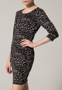 Leopardmönstrad klänning med en figurnära silhuett, trekvartsärmar och en mjuk textur i nyanser av svart och beige.