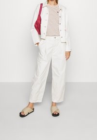 Vit denimjacka över en randig skjorta, kombinerad med vita vida byxor och beige sandaler med tvärband. Rosa axelväska som accent.