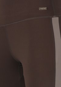 Leggings marroni realizzati in materiale elasticizzato, con un pannello grigio a contrasto, cuciture piatte e un piccolo etichetta con logo lungo l'elastico in vita.