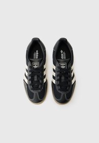 Zwarte Adidas sneakers met witte strepen, met een mesh ontwerp, veters en rubberen zolen, plat weergegeven tegen een witte achtergrond.