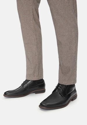 Juodos odinės elegantiškos bateliai su lygiu paviršiumi, apvalia nosimi ir raištelių dizainu, derinami su languotomis kelnėmis šviesiomis ir tamsiomis spalvomis.