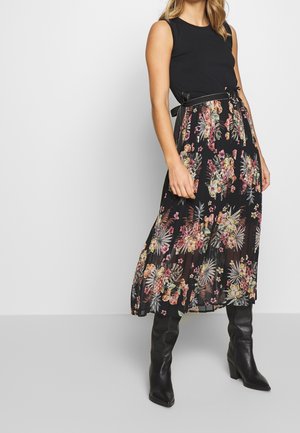 Sukienka w kwiaty z dopasowanym czarnym góram i długą, warstwową spódnicą ozdobioną intensywnie kolorowymi kwiatami na czarnym tle. Czarne kozaki do kolan.