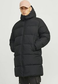 Abrigo acolchado negro con cuello alto, cierre de cremallera y diseño acolchado sin patrón. Cuenta con capucha y bolsillos laterales. Tejido liviano.