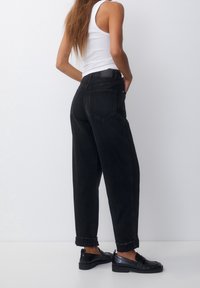 Černé džíny s vysokým pasem a uvolněným střihem, s ohrnutými nohavicemi a dvěma zadními kapsami. Materiál se zdá být pevný a texturovaný.