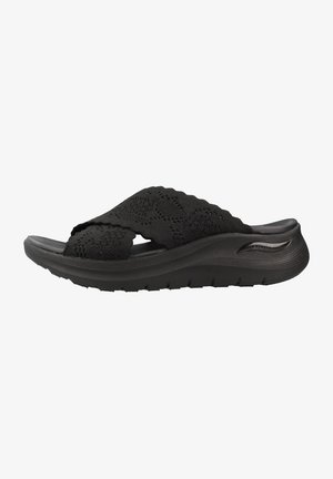 Sandalia negra tipo slip-on con correas de punto texturizadas y una suela gruesa acolchada diseñada para la comodidad y soporte.