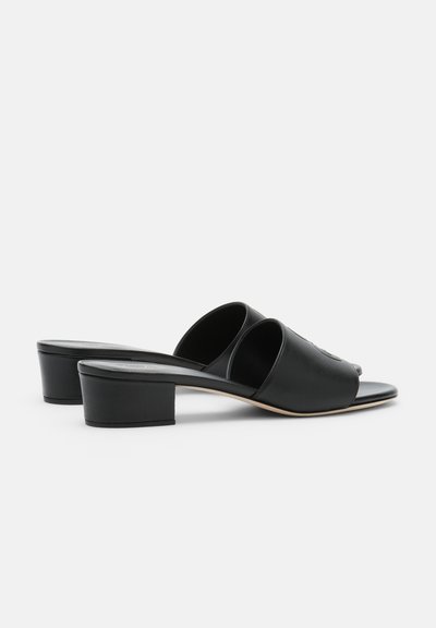 Sandales noires en cuir à talons bas, ouvertes à l'avant, à enfiler, avec deux larges brides et un talon bloc, sur un fond blanc uni.