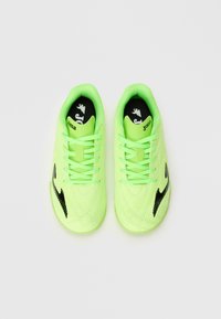 Un par de zapatillas deportivas de color verde neón con un logo negro en los laterales y "Joma" impreso en la lengüeta, mostradas sobre un fondo blanco.