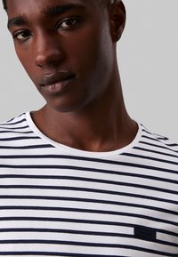 T-shirt a righe navy e bianche in cotone, con scollatura a girocollo e un piccolo cartellino rettangolare con il logo Calvin Klein sul petto.