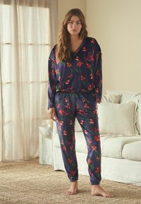 Tumesinise värviga pidžaamakomplekt pehmest kangast, millel on lillemustrid. Pika varrukaga särk on V-kaelusega ja lõdva istuvusega; püksid on elastsete mansettide ja vöökohaga.